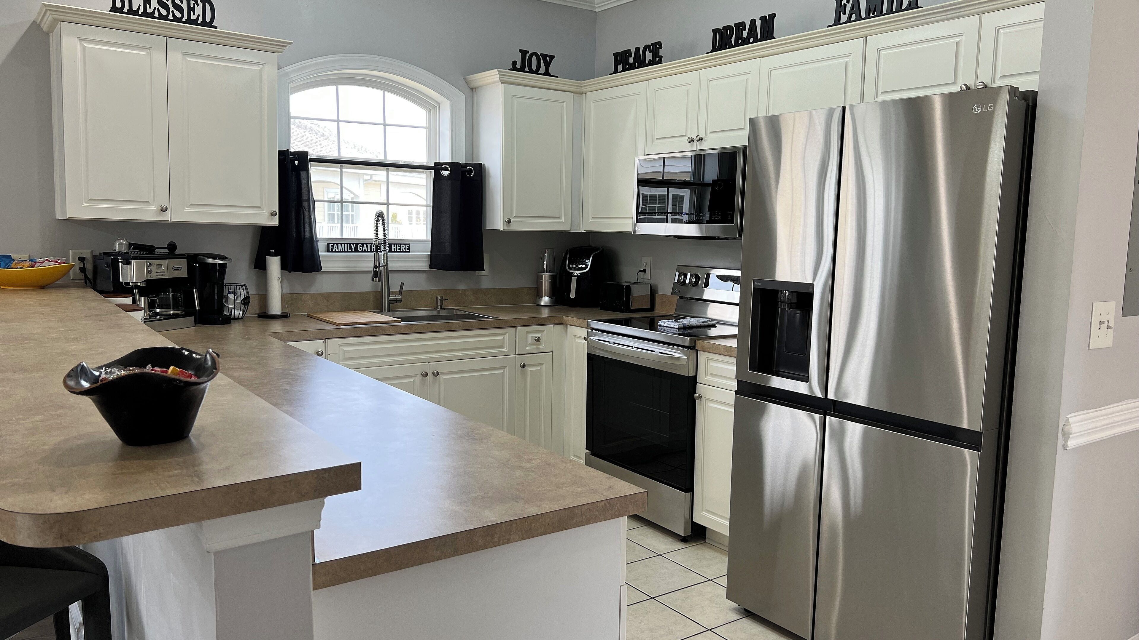 A modern kitchen with white cabinetry, stainless steel appliances, and a large island with a black bowl.
