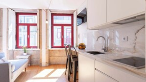 Eine kleine Küche mit Spüle, einem Fenster mit roten Fensterläden und einer gemütlichen Sitzecke.