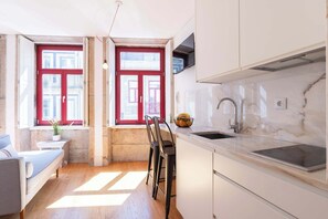 A compact kitchen with a sink, a window with red shutters, and a small seating area. - Modern Studio with Terrace & Jacuzzi by HostWise (Porto)