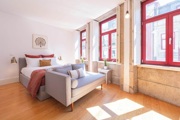 A modern bedroom with a bed, a sofa, a small table, and a window with red shutters. - Modern Studio with Terrace & Jacuzzi by HostWise (Porto)