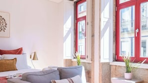 Ein modernes Hotelzimmer mit Schlafsofa, einem kleinen Tisch und einem Fenster mit roten Rollläden.