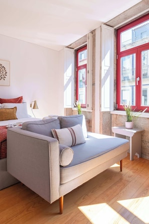 A modern hotel room with a sofa bed, a small table, and a window with red shutters. - Modern Studio with Terrace & Jacuzzi by HostWise (Porto)