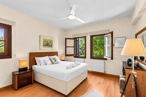 A bedroom with a bed, bedside tables, a ceiling fan, windows, and artwork.