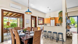 A dining area with a wooden table, wicker chairs, and a kitchen in the background.