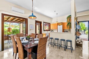 A dining area with a wooden table, wicker chairs, and a kitchen in the background.