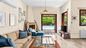 A living room with a beige sofa, blue armchairs, a glass coffee table, a fireplace, a TV, and a view of a swimming pool.