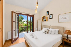 A bedroom with a bed, a nightstand, a lamp, a window, and a door leading to a balcony.