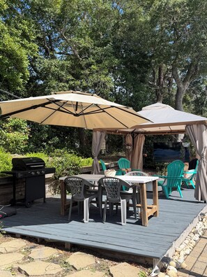 Une terrasse extérieure équipée d’un barbecue, de tables, de chaises et de parasols.