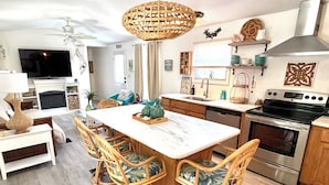 Una cocina moderna con una isla central, taburetes de bar, horno empotrado y un comedor con televisor y chimenea.