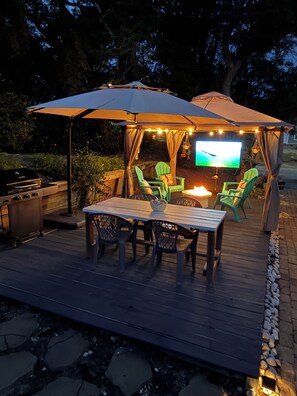 An outdoor patio with a table and chairs, a grill, and a television screen. - The Mermaids House- Kayaks + Canoe, Centrally located, Pet Friendly (Emerald Isle)