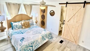 Un dormitorio con una cama, un ventilador de techo, una puerta de madera y una ventana con cortinas.