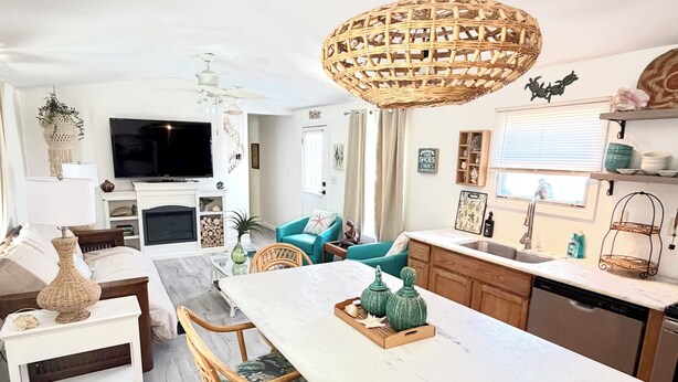 Una cocina moderna con una isla central, comedor con sillas de mimbre y un televisor grande en la sala de estar.
