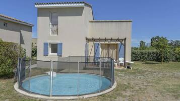 A two-story building with a swimming pool, a covered patio, and a fenced area.