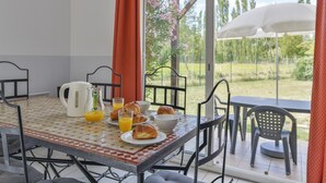 A breakfast table with croissants, juice, and a kettle, set in a room with a view of trees and a patio. - Provence Villa for 8 With Private Pool (Saint-Saturnin-les-Avignon)