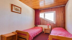 A room with two wooden beds, a window with curtains, a radiator, and a framed picture on the wall. - Cosy Apartment 150 m From ski Slopes (Les Deux Alpes)
