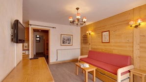 A wooden interior with a red sofa, wooden tables, a TV, and a chandelier. - Cosy Apartment 150 m From ski Slopes (Les Deux Alpes)