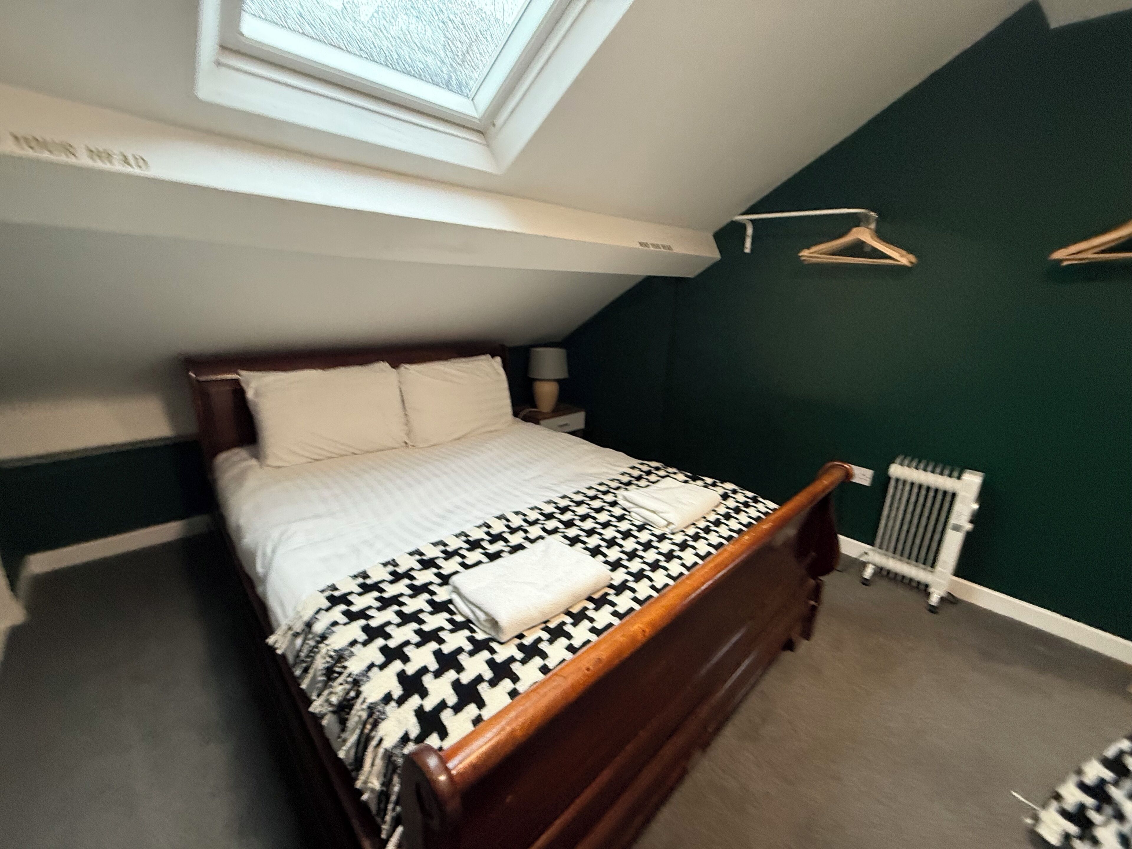 Une chambre avec un lit, une lucarne, un radiateur et un porte-vêtements suspendu.