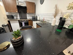 A modern kitchen with a black countertop, stainless steel appliances, wooden cabinets, and a potted plant. - Cosy Apartment within a short walk to the nightlife and the business district (Liverpool)