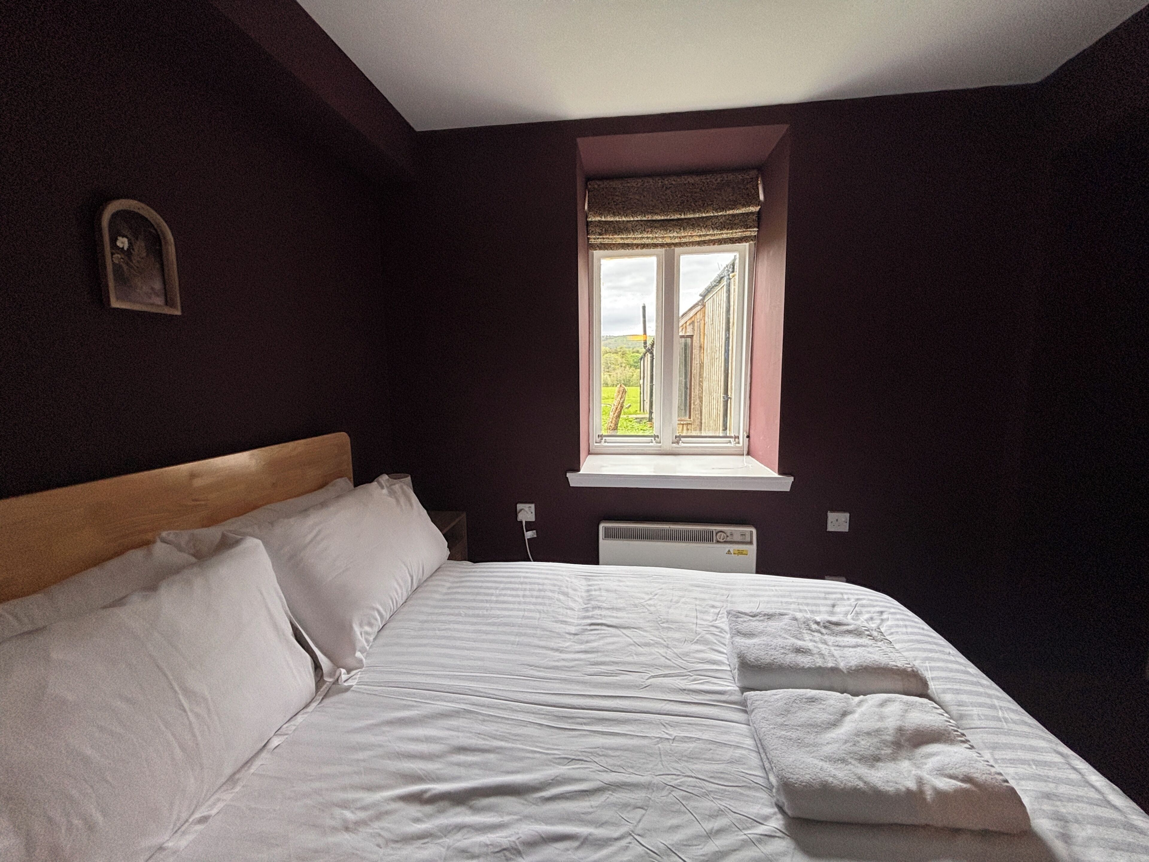 Une chambre avec un lit, une fenêtre donnant sur un beau paysage et un radiateur fixé au mur.