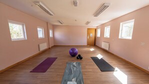 A spacious room with wooden flooring, a yoga mat, a purple exercise ball, and dumbbells.
