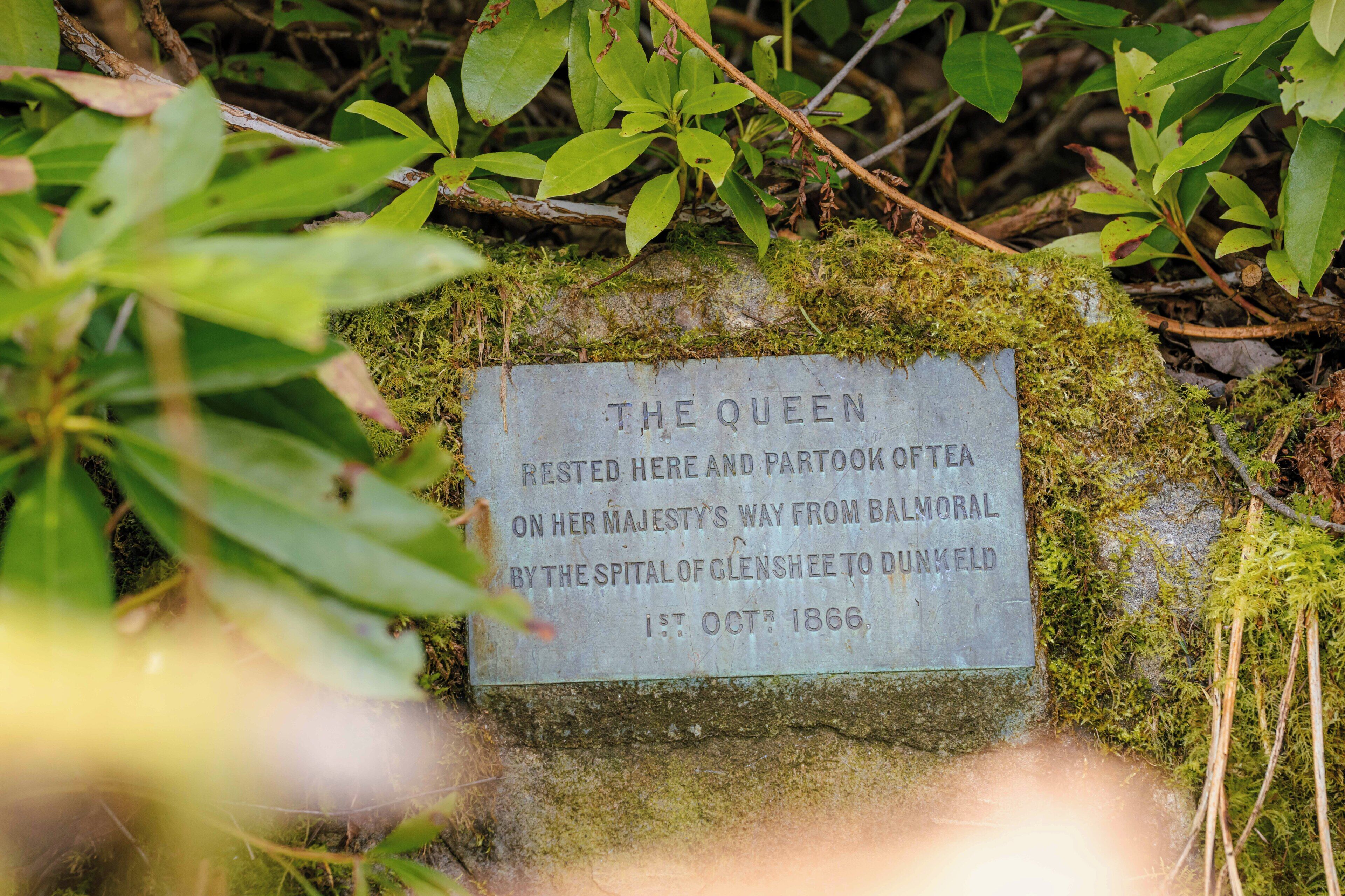 A historical plaque on a moss-covered rock with text about Queen Victoria's visit.
