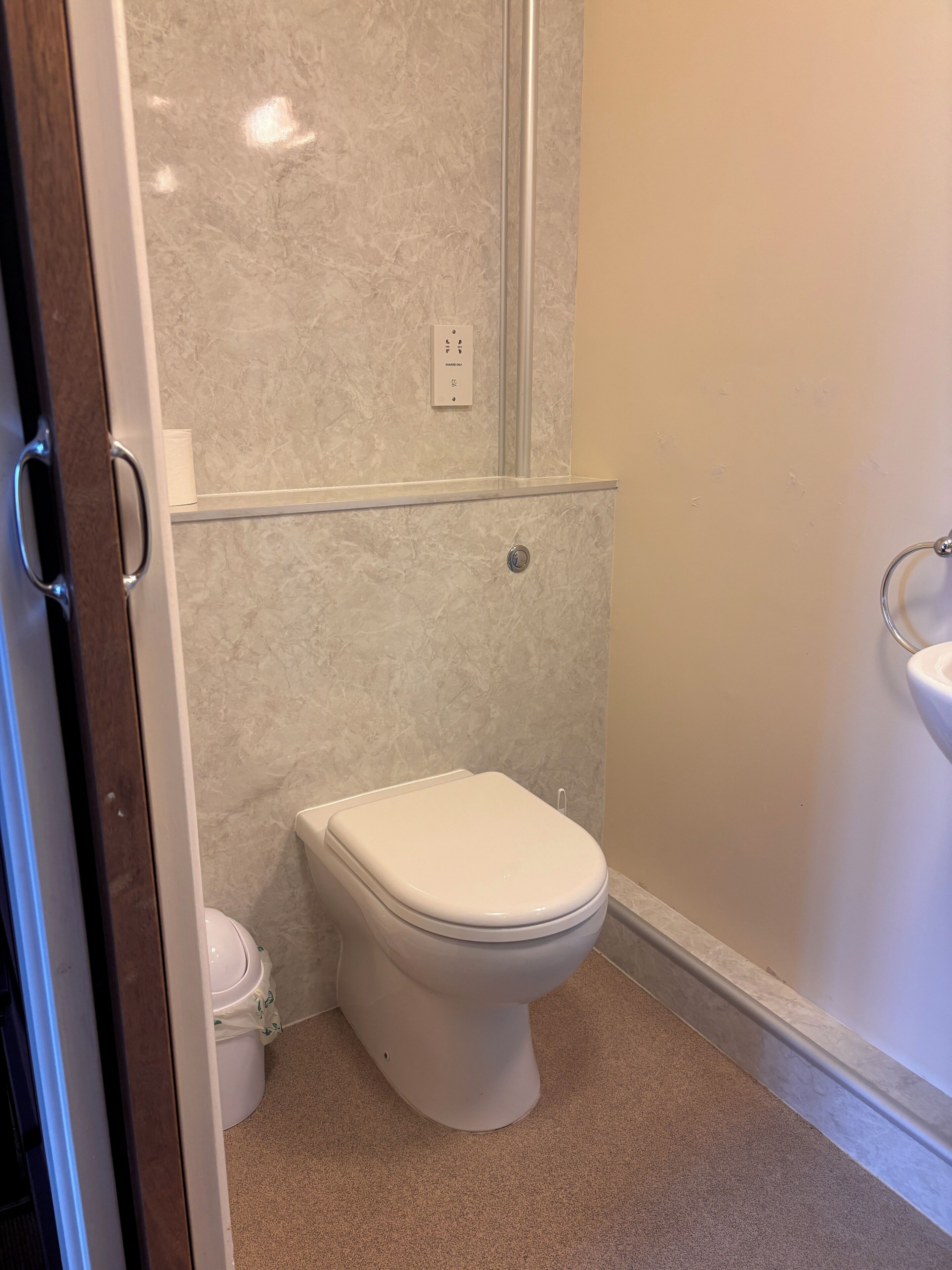 Ein Badezimmer mit Toilette, einer fest installierten Steckdose und einem Waschbecken.