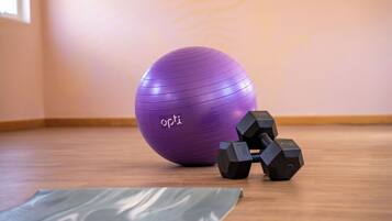 A purple exercise ball, two black dumbbells, and a yoga mat on a wooden floor in a room with a light-colored wall.