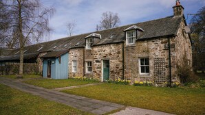 A stone building with a blue door, a chimney, and a small garden with yellow flowers.