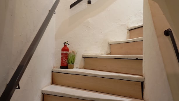 Una escalera con escalones de madera, un extintor y una pequeña planta en maceta.