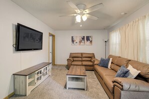 A living room with a brown leather sofa, a wooden coffee table, a TV mounted on the wall, and a ceiling fan. - Game Day Getaway! Delightful 3-bedroom house with AC in charming Independence (Independence)