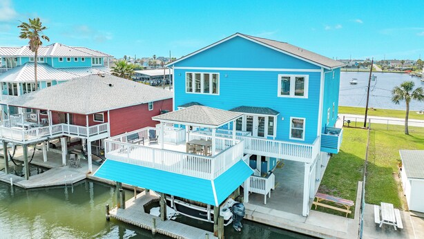 A waterfront property with a blue house, a dock, and a small boat. - Canal Home w/ 2 Living Areas, 2 Levels of Deck, Hot Tub, Game Room, Pet Friendly (Galveston)