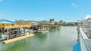 A waterfront property with a dock, a covered seating area, and a view of the water. - Canal Home w/ 2 Living Areas, 2 Levels of Deck, Hot Tub, Game Room, Pet Friendly (Galveston)