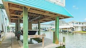 A waterfront dock with a covered seating area, boats, and adjacent buildings. - Canal Home w/ 2 Living Areas, 2 Levels of Deck, Hot Tub, Game Room, Pet Friendly (Galveston)