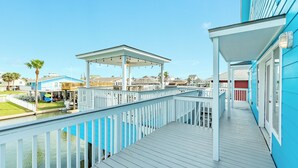 A waterfront property with a wooden deck, a covered patio, and a view of the water and neighboring houses. - Canal Home w/ 2 Living Areas, 2 Levels of Deck, Hot Tub, Game Room, Pet Friendly (Galveston)
