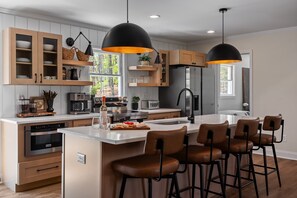 A modern kitchen with wooden cabinets, a central island, bar stools, and pendant lighting. - Thornberry Cottage - Time To Relax (Dahlonega)