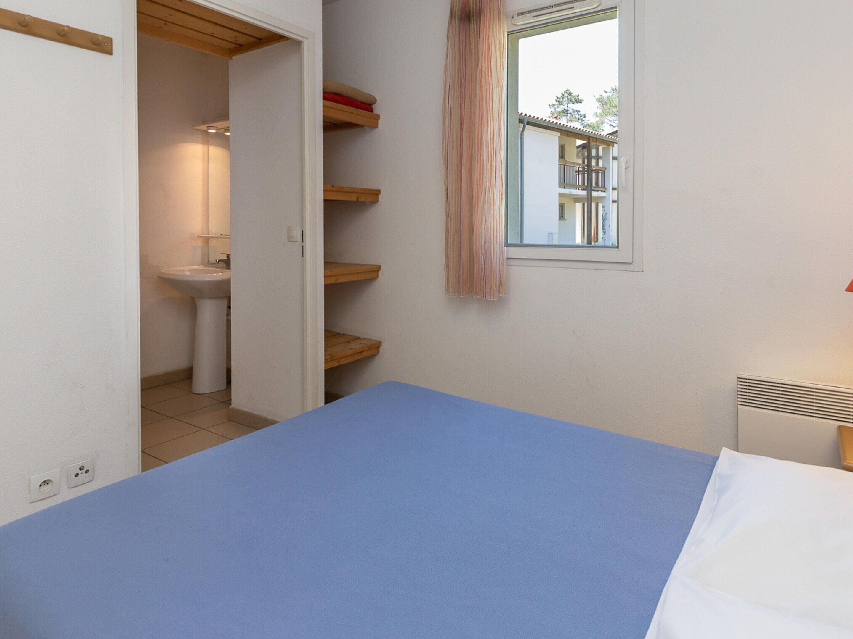 A bedroom with a bed, a window with a view, a sink, and a wooden shelf.