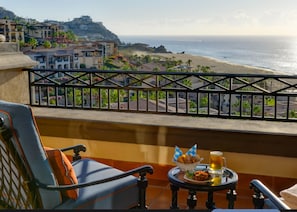Uma varanda com vista para a praia, uma mesa com comida e bebidas, e uma cadeira.