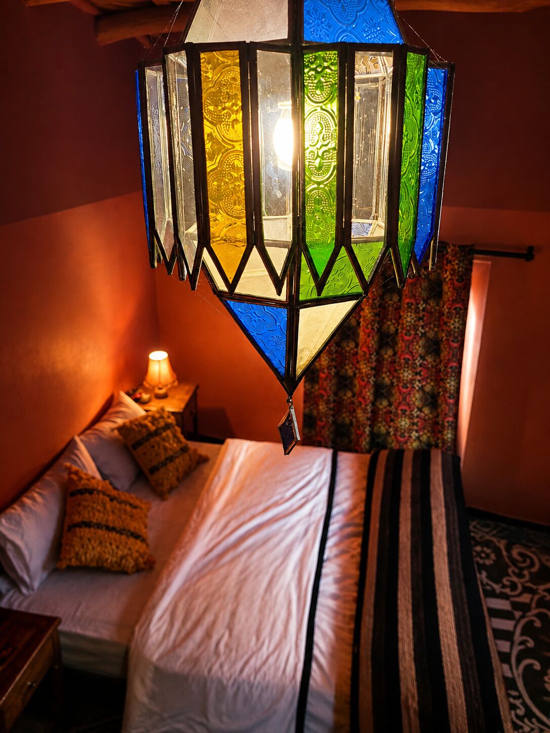 Een kamer met een bed, nachtkastje, lamp en hanglamp.