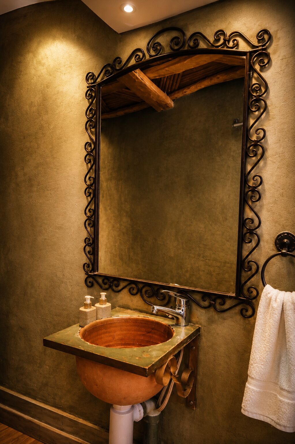 A bathroom with a copper sink, a mirror with ornate black frame, and a towel hanging on a rack.