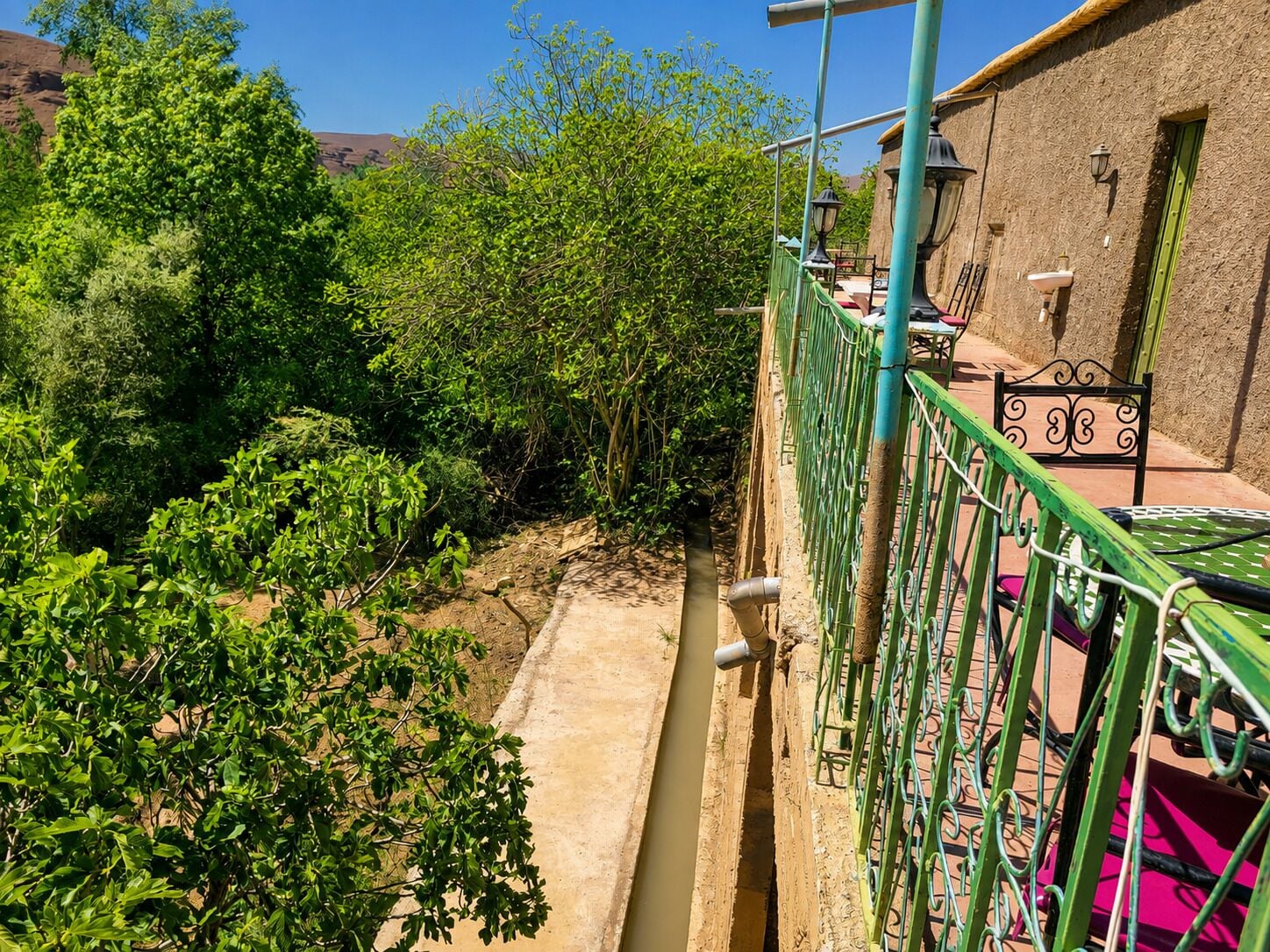 A balcony with a view of a garden and a building with a green door.