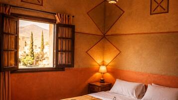 Una habitación acogedora con cama, mesita de noche con lámpara, ventana con cortinas y techo de madera.