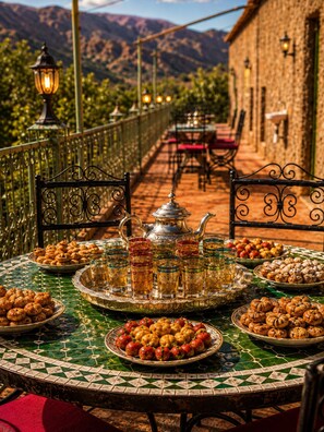 A table set with traditional Moroccan tea, pastries, and fruits, with a view of mountains in the background.