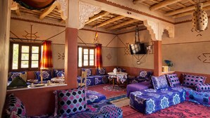 A traditional room with wooden beams, patterned cushions, and a television. - dar moha dades (Ait Sedrate Jbel El Soufla)