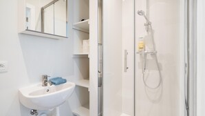 Ett badrum med en dusch som är avskärmad med glasväggar, ett vitt handfat och en spegel.