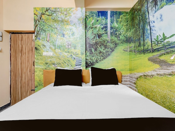Una cama con ropa blanca y almohadas negras, un armario de madera y un tapiz grande con motivos forestales en la pared.