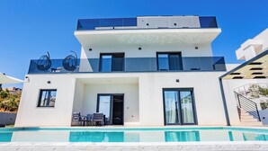 Et moderne hus med to etager, en swimmingpool, store vinduer og en balkon.