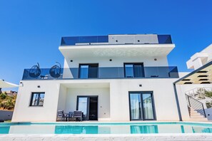 Ein modernes, zweistöckiges Haus mit Swimmingpool, großen Fenstern und einem Balkon.