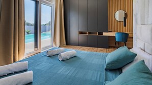Et moderne hotelværelse med en stor seng, et skrivebord, en stol, et rundt spejl og udsigt til en swimmingpool.