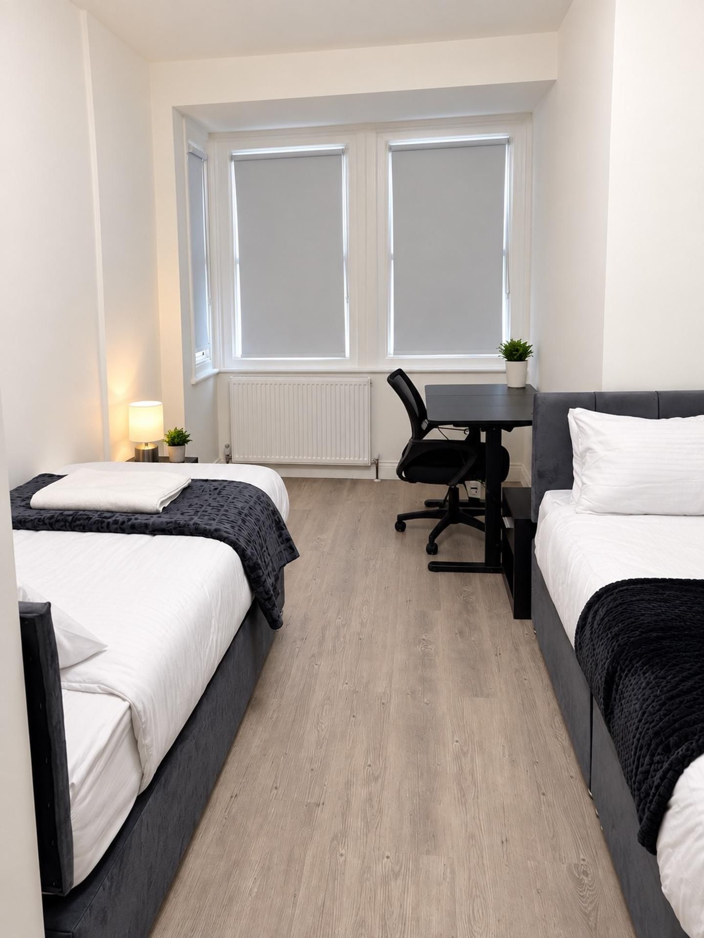 A hotel room with two beds, a desk, and a window.