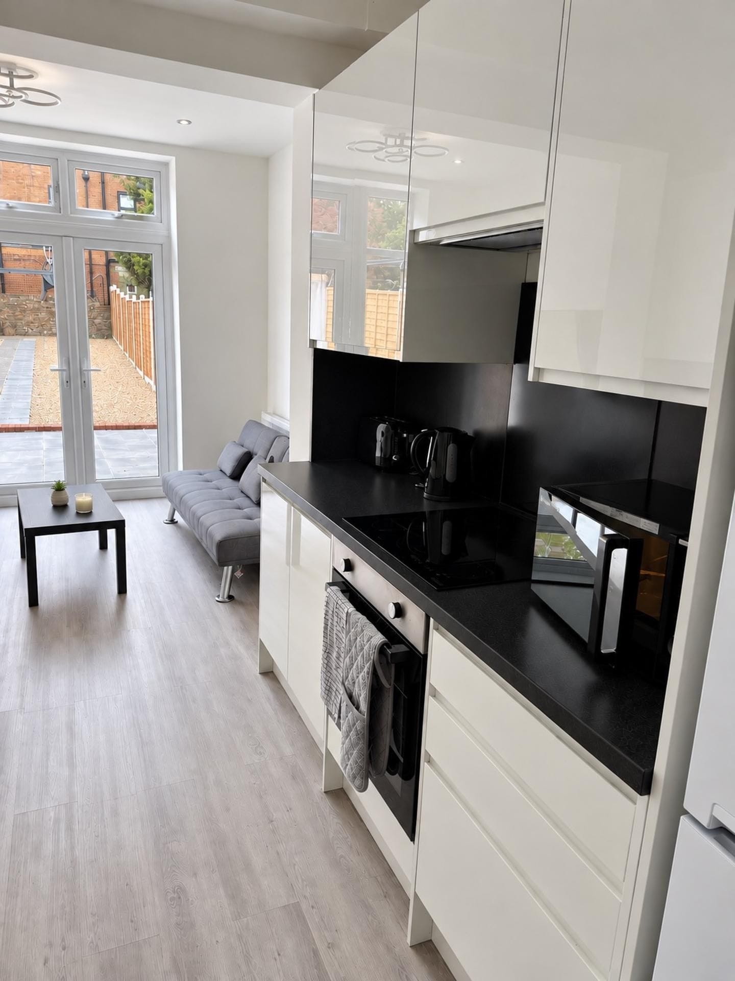 A modern kitchen with white cabinets, a black countertop, and a built-in oven. There is a grey sofa and a small table with a candle.